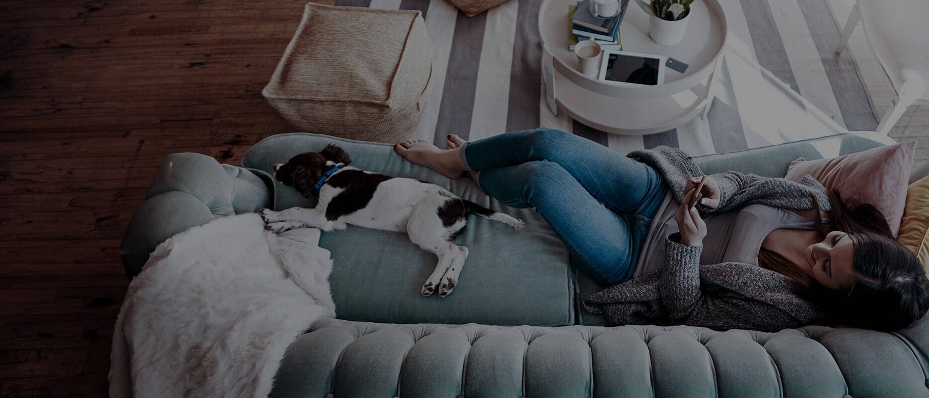 Foto av kvinne som ligger på sofa og sufer på mobilen ved siden av en hund